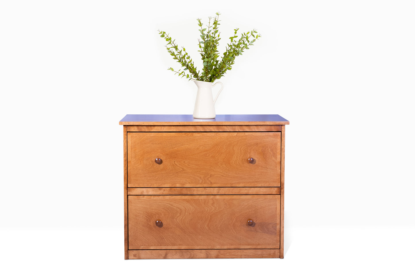 Front view of two drawer lateral file cabinet built in birch with wood knobs, in a light brown stain color, and with a pitcher with decorative greens sitting on top.