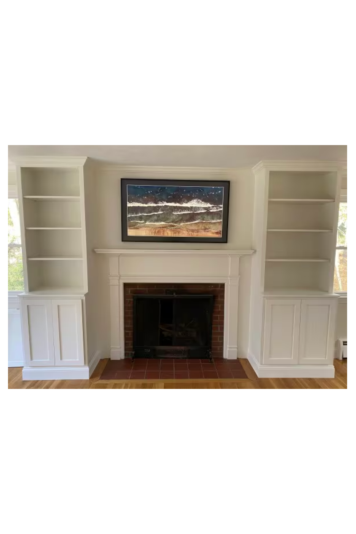 Two step back bookcase hutches built in birch painted white with doors and base molding on either side of a fireplace in someone's home.