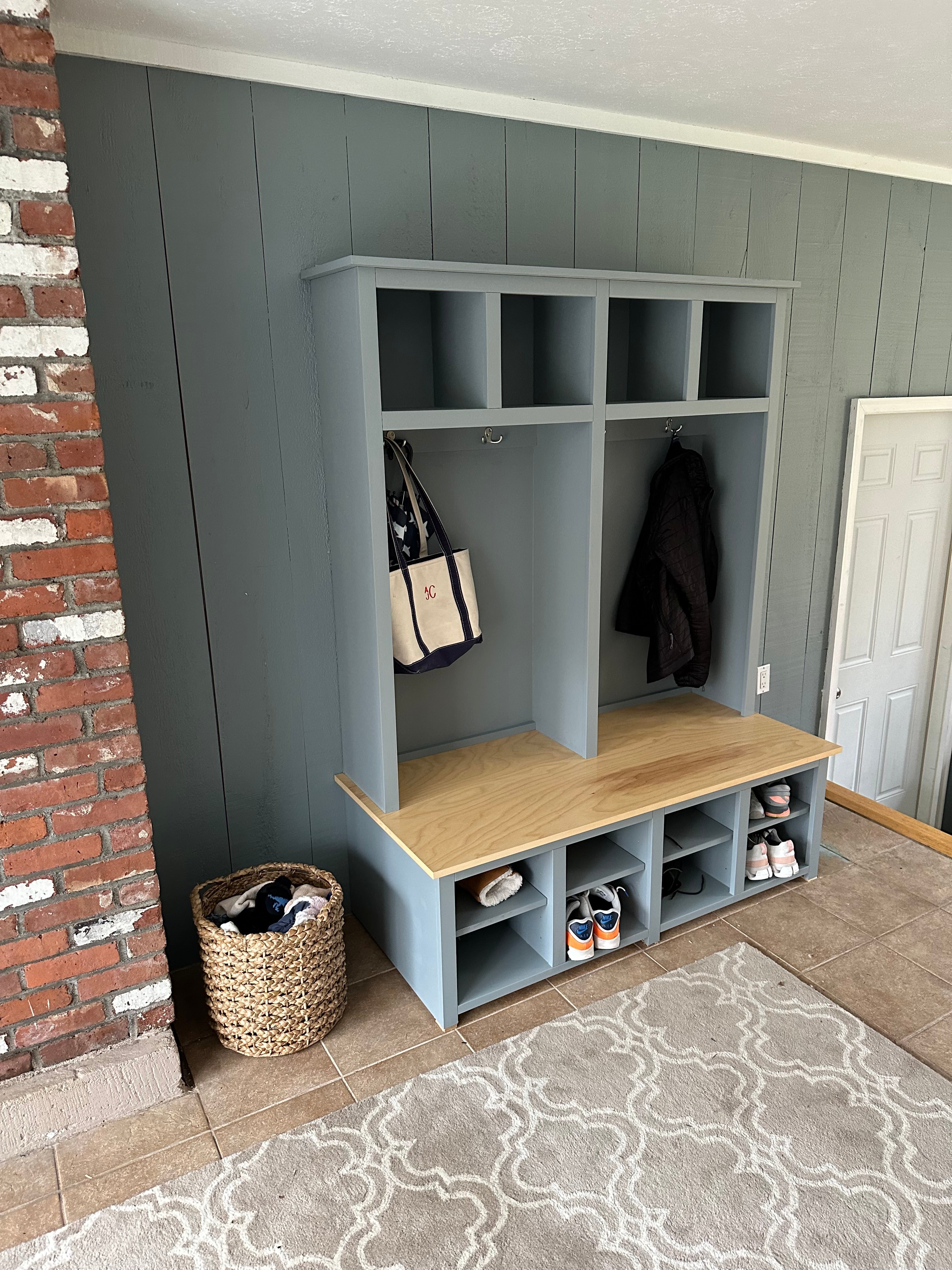Custom hall tree in front entryway of home built in birch with open storage in the base, a section for hanging coats and bags, and upper cubby storage painted a sage green.